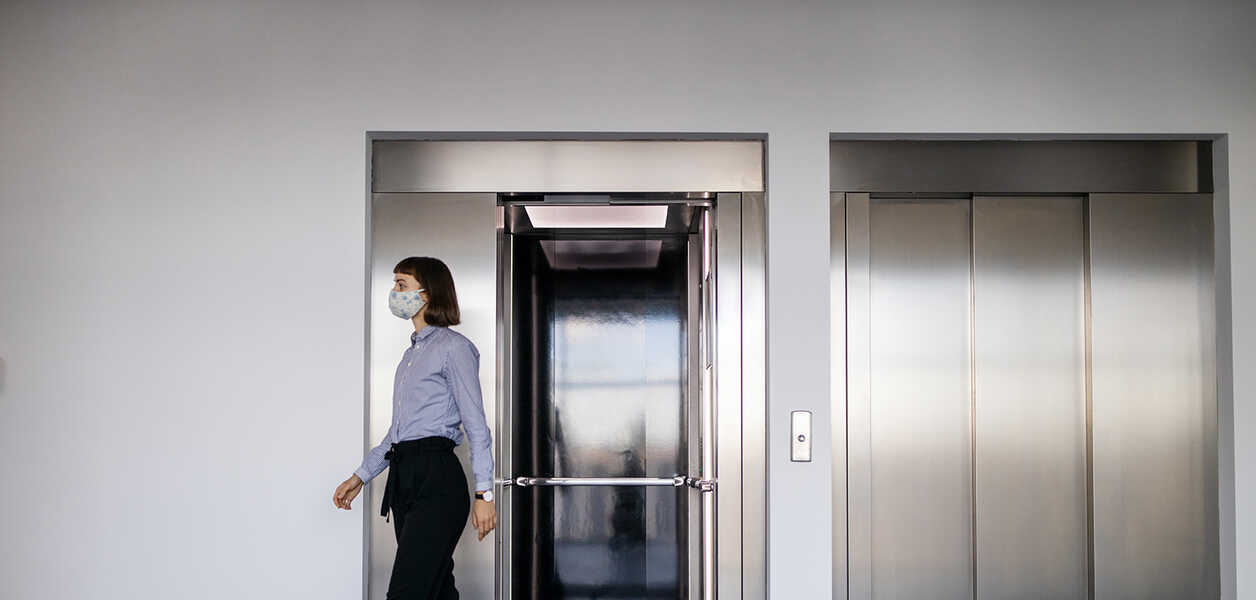 Femme portant un masque, sortant d’un ascenseur