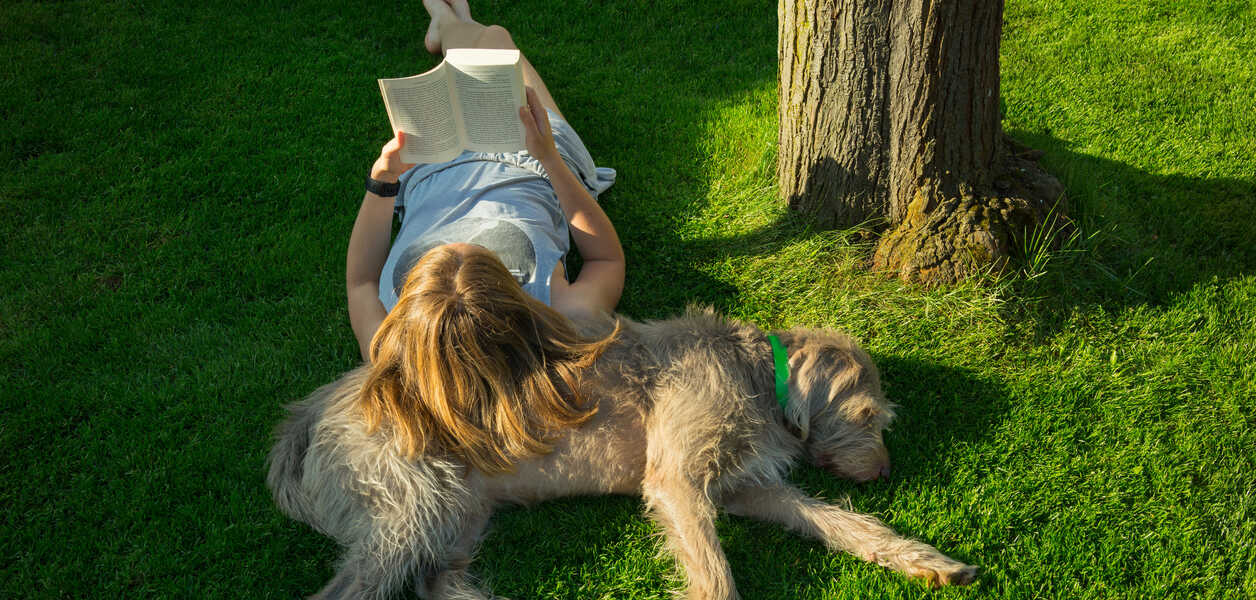 Femme lisant un livre, étendue sur le gazon avec son chien