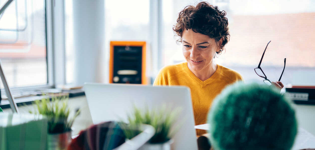 Woman smiling at computer holding glasses
