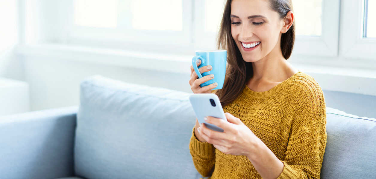 Woman holding a coffee while scrolling through an employee program on her phone.