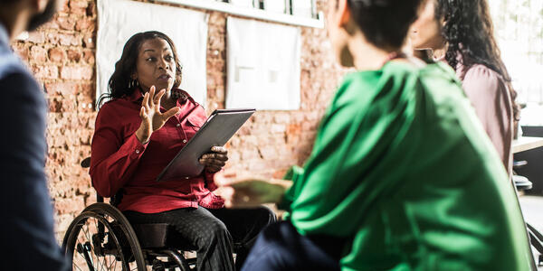 Woman in wheelchair presenting to three people seated around her