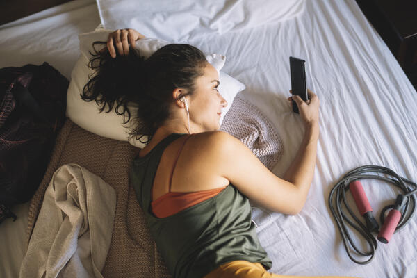 Femme étendue sur son lit, parlant au téléphone, avec une corde à sauter à ses côtés