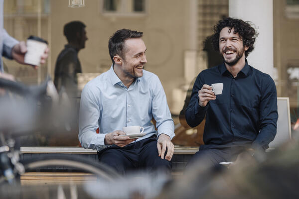 Two men laughing enjoying espressos outside