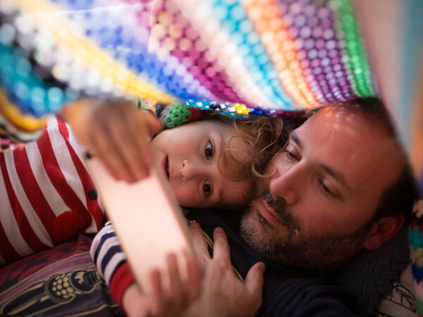 Dad and daughter look at phone in blanket fort