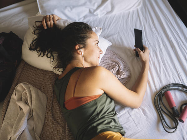 Femme étendue sur son lit, parlant au téléphone, avec une corde à sauter à ses côtés