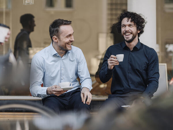 Deux hommes qui rient, tout en prenant un espresso à l’extérieur